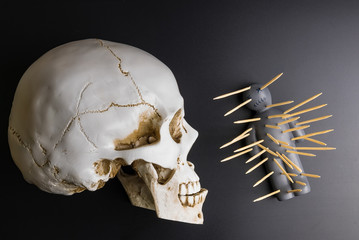 Voodoo doll with pins stuck into it and white skull on a black background with dramatic lighting.