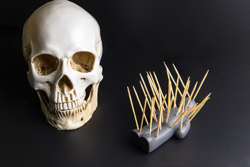 Voodoo doll with pins stuck into it and white skull on a black background with dramatic lighting.