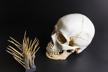 Voodoo doll with pins stuck into it and white skull on a black background with dramatic lighting.
