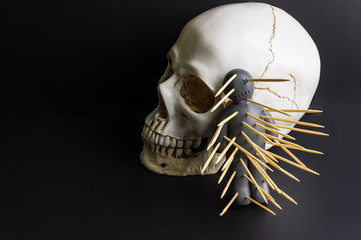 Voodoo doll with pins stuck into it and white skull on a black background with dramatic lighting.