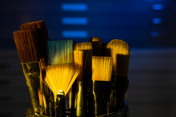 Container of artist brushes with creative lighting and file cabinet in background