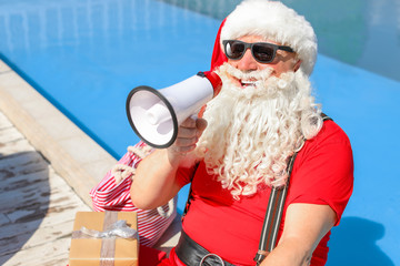 Obraz premium Cool Santa Claus with megaphone near swimming pool at resort