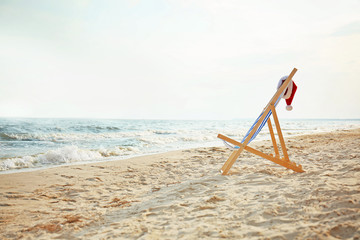 Beach chair with Santa Claus hat on sea coast. Christmas vacation