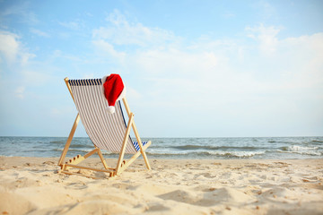 Beach chair with Santa Claus hat on sea coast. Christmas vacation