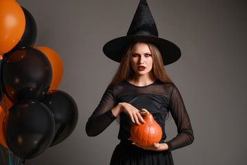 Beautiful woman dressed as witch for Halloween on grey background