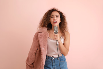 Beautiful African-American female singer with microphone on color background