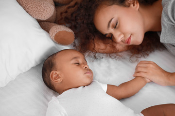 Young African-American woman and her baby sleeping on bed