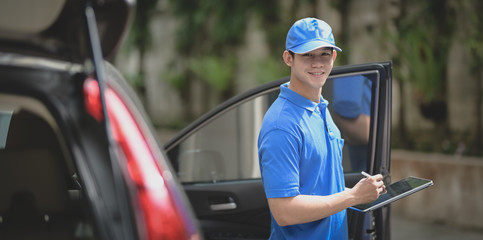 Delivery man preparing parcel box to customer while checking orders on tablet and smiling to the camera