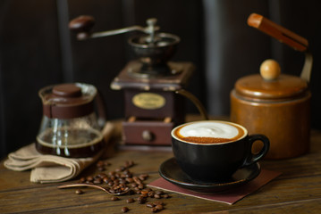 Closeup top view of hot cappucino cup with selective focus on coffee beans on wooden table with blurred grinder background