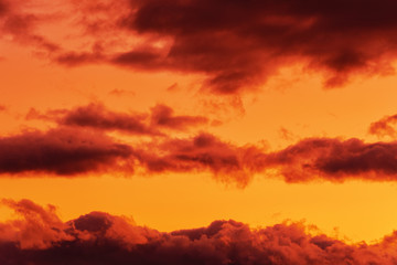 Fototapeta na wymiar Orange clouds glowing by disappearing rays at sunset floating across yellow sky. Summer amazing view of skyscape, natural meteorology background. Soft focus, motion blur clouds.