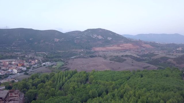 Drone Aerial shot, flying over a pine trees wood towards the mine of Monte Poni on the opposite hill in Iglesias, Sardinia, Italy