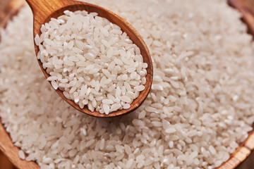 Uncooked rice in a wooden spoon over the bowl  of rice. Close up.