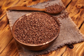 Uncooked buckwheat in a wooden bowl with the wooden spoon full of buckwheat, rustic background. Close up.