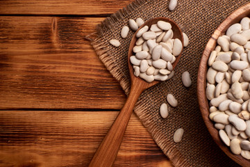 White beans in a wooden bowl with the wooden spoon full of white beans, rustic background. Top view. Copy space in the left.