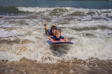 Father or instructor teaching his 5 year old son how to surf in the sea on vacation or holiday. Travel and sports with children concept. Surfing lesson for kids