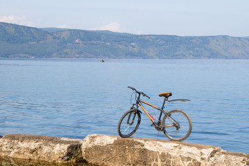 Fototapeta premium Bicycle standing on stones against backdrop of Lake Baikal.