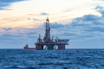 Drilling rig and supply boat in the sea at sunset