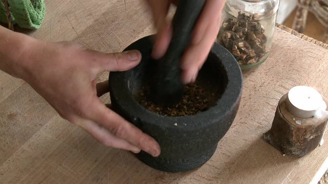 Handheld, close up shot of a person crushing peppercorns with mortar and pestle.