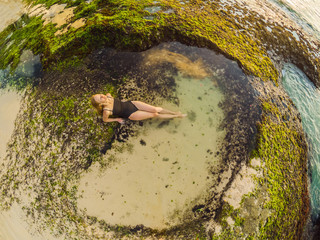 Young woman tourist on Pantai Tegal Wangi Beach sitting in a bath of sea water, Bali Island, Indonesia. Bali Travel Concept
