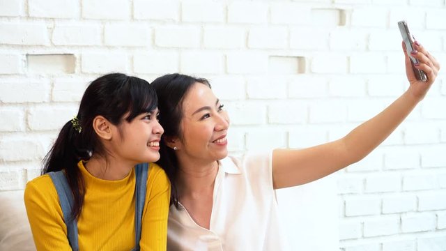 Happy Asian teenage daughter and middle-aged mother taking selfie or video calling