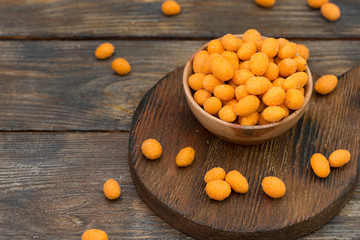 Roasted peanuts in red chili pepper in a wooden bowl on a wooden table
