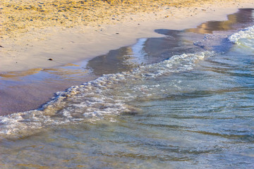 Clear sea water washes the sandy shore of the beach.