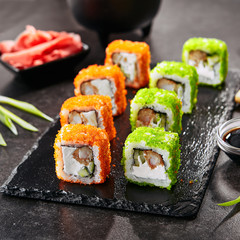 Macro shot uramaki sushi roll with rice, cream cheese, fried shrimp, cucumber, flying fish caviar and nori. Fresh colorful rolls in Japanese restaurant with chopsticks closeup