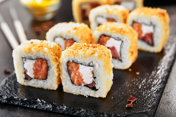 Macro shot of hot crispy tempura maki sushi rolls with cream cheese, raw salmon, tomato and nori seaweed. Deep fried uramaki roll set on natural black stone slate background closeup