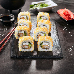 Macro shot of hot crispy ebi tempura maki sushi rolls with cream cheese, king prawn, chuka kelp salad and nori. Deep fried uramaki roll set on natural black stone slate background closeup