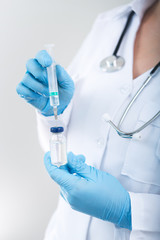 Woman doctor holding flu vaccine and syringe in hands on a white background