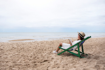 Fototapeta na wymiar A beautiful woman lying down and reading book on the beach chair with feeling relaxed