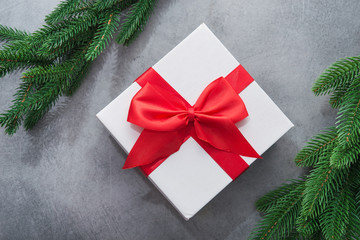 Christmas white box present with red ribbon and fir tree branch