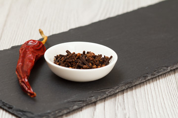 Cloves in a bowl and dry red pepper on stone cutting board