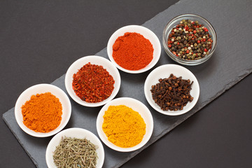 Various ground spices and herbs on stone cutting board.