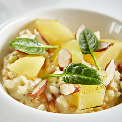 Exquisite Serving White Restaurant Plate of Risotto with Gorgonzola Cheese, Raisins, Almonds and Baked Pear Close Up. Beautiful Delicacy Italian Fruit Paella on Dark Stone and Leaves Background