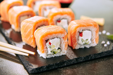 Beautiful Philadelphia Sushi Rolls Set with Salmon and Cream Cheese and Cuccumber on Black Slate Plate Close Up. Uramaki, Nori Maki or Futomaki Sushi with Trout Fillets, Soy Sauce and Wasabi
