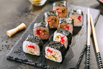 Macro shot of sushi roll in Japanese restaurant with chopsticks closeup. Sushi rolls with rice, fried salmon, flying fish caviar, cucumber and spicy sauce