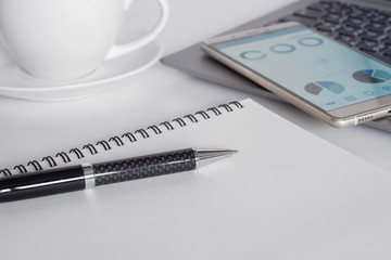 White office desk with laptop, coffee, mobile phone with business analysis graph, notebook with pen with copy space for your text message.
