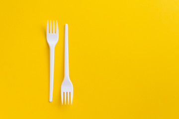 White plastic forks on vibrant yellow background. Flatlay. Fast food, eco and no plastic concept. Copy space.