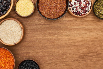 top view of bowls with diverse beans, red lentil, couscous and buckwheat on wooden surface
