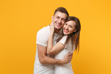 Beautiful young couple two friends guy girl in white empty blank design t-shirts posing isolated on yellow orange background studio portrait. People lifestyle concept. Mock up copy space. Hugging.