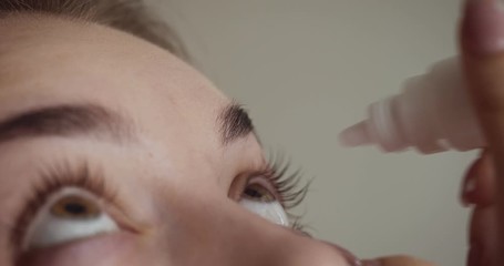 Young woman drops eyes with eyedropper.