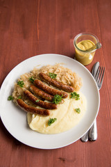 Kleine Bayrische Nürnberger Rostbratwürste mit Sauerkraut, Kartoffelpüree und Senf auf Holz Tisch Hintergrund
