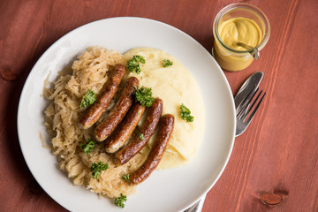 Kleine Bayrische Nürnberger Rostbratwürste mit Sauerkraut, Kartoffelpüree und Senf auf Holz Tisch Hintergrund