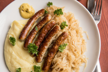 Kleine Bayrische Nürnberger Rostbratwürste mit Sauerkraut, Kartoffelpüree und Senf auf Holz Tisch Hintergrund