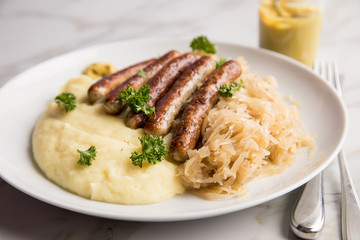 Kleine Bayrische Nürnberger Rostbratwürste mit Sauerkraut, Kartoffelpüree und Senf auf Marmor Tisch Hintergrund