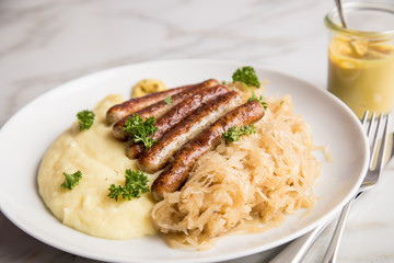 Kleine Bayrische Nürnberger Rostbratwürste mit Sauerkraut, Kartoffelpüree und Senf auf Marmor...