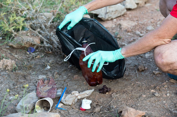 Closeup of hand picking up drinking plastic bottle waste into black garbage bag. Ecology and Environmental concerns. Recycling and waste reduction techniques. Eco friendly earth world disaster relief.
