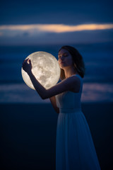 Naklejka premium delikatny obraz anioła, dziewczyny z księżycem w rękach na nocnej plaży. fotografia artystyczna. Bajka i zagadka. Astrologia i znaki zodiaku.