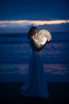 delicate image of an angel, a girl with the moon in her hands on the night beach. artistic photography. Fairy tale and riddle. Astrology and zodiac signs.